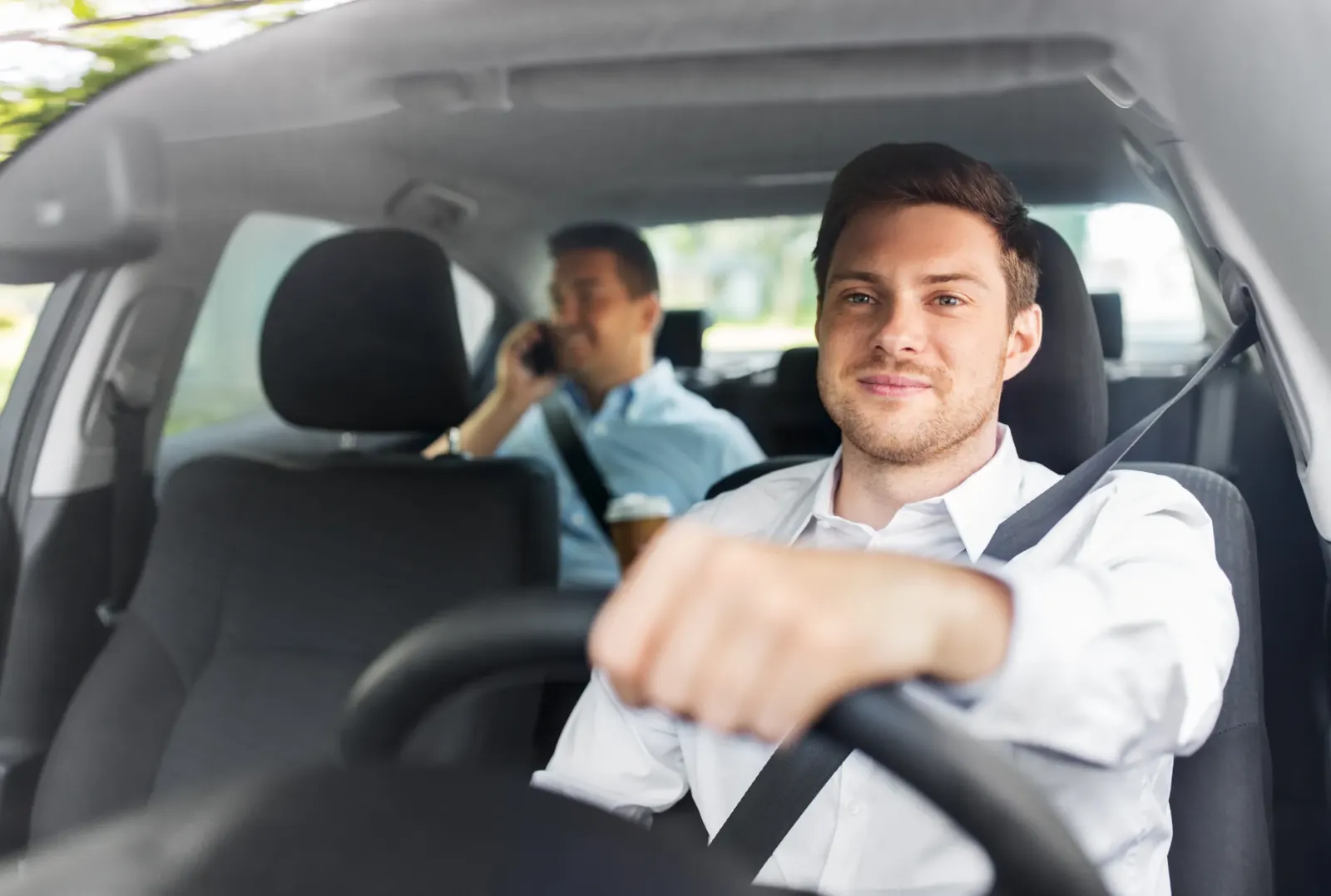 Driver seated at the wheel of a passenger car with the shoulder belt fastened across the torso.