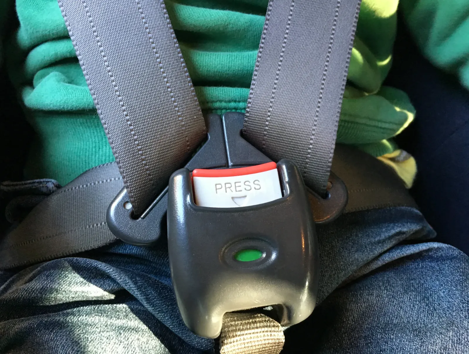Multi-point harness restraint with shoulder straps meeting a central buckle on a seated occupant.