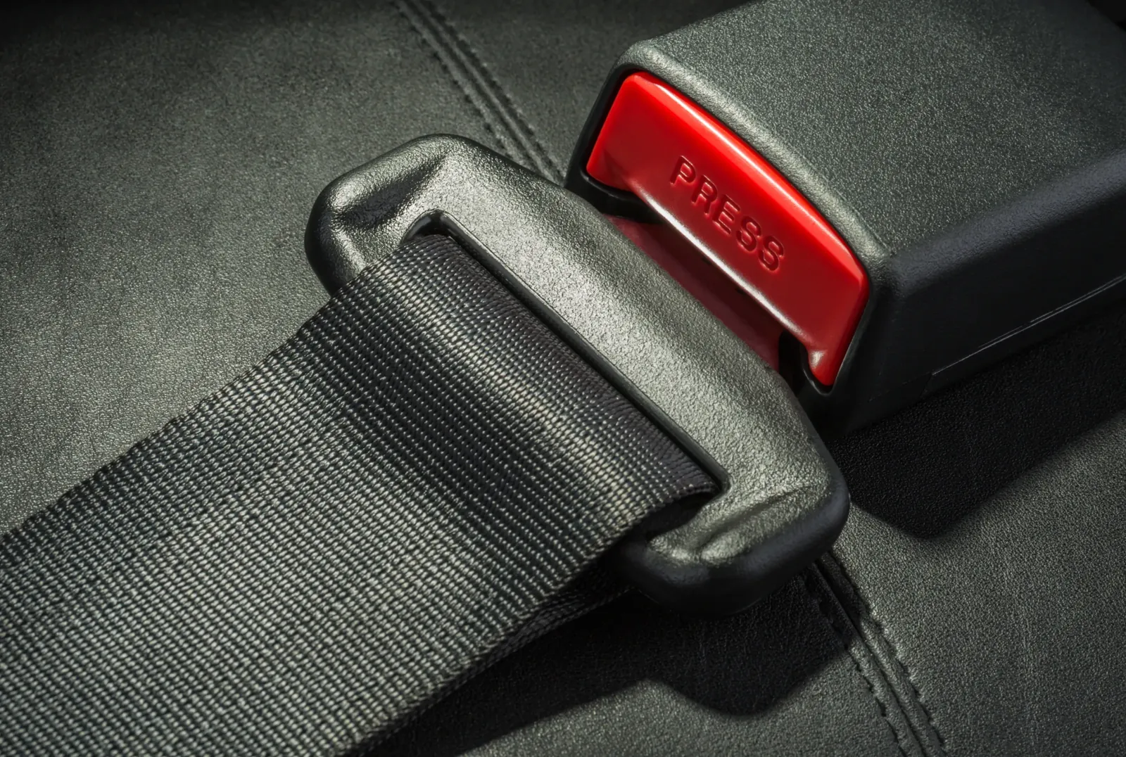 Automotive seat belt buckle with a red release button, with the webbing tongue engaged in the latch.